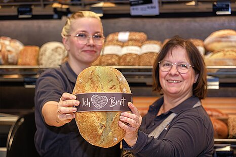 Zwei Mitarbeiterinnen der Firma "Braune" halten ein Brot mit der Banderole "Ich liebe Brot" um für neue Mitarbeiter-innen zu werben